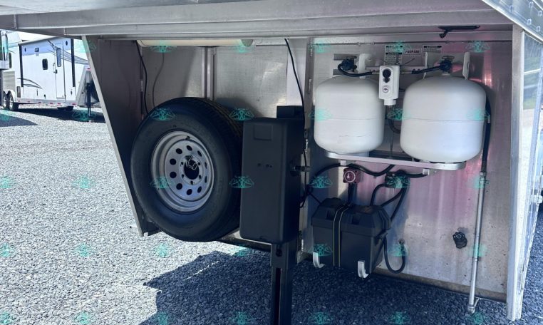 Underbelly of a trailer showing a spare tire, two propane tanks, and a battery box mounted inside the rear area.