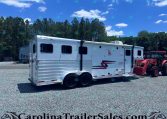 White horse trailer on a gravel lot with a forested backdrop and a red tractor nearby under a bright blue sky.