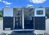 Open horse trailer with divider inside, showing empty stalls and seating, blue sky visible outside.