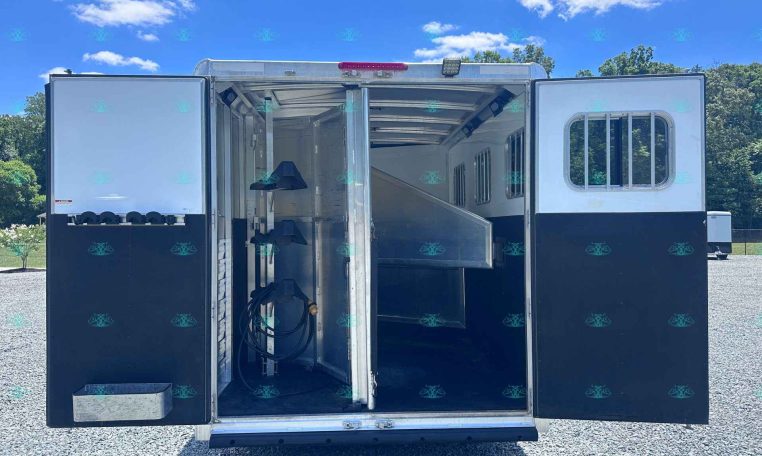 Open horse trailer with divider inside, showing empty stalls and seating, blue sky visible outside.