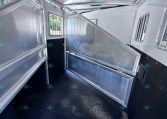 Interior of a silver aluminum trailer with a lowered ramp and divider, window with bars visible on the side.