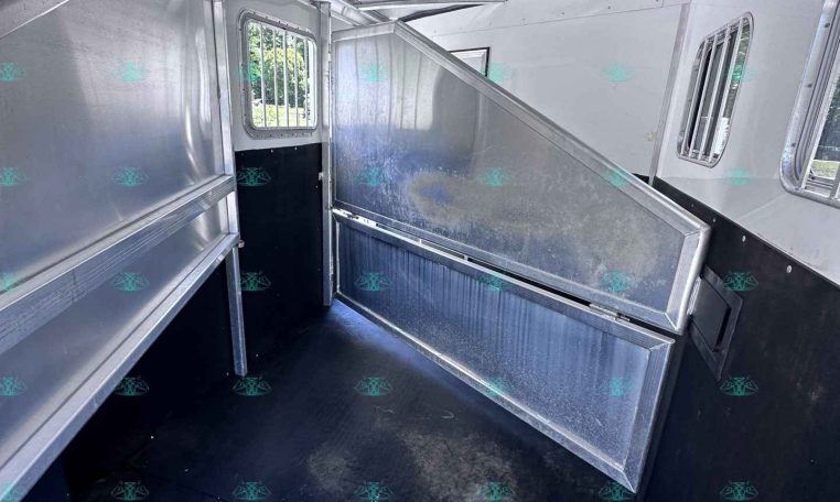 Interior of a silver aluminum trailer with a lowered ramp and divider, window with bars visible on the side.