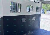 Interior of a white horse trailer with barred windows along the walls and ceiling-mounted lights visible inside