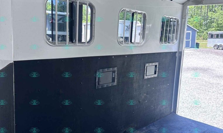 Interior of a white horse trailer with barred windows along the walls and ceiling-mounted lights visible inside