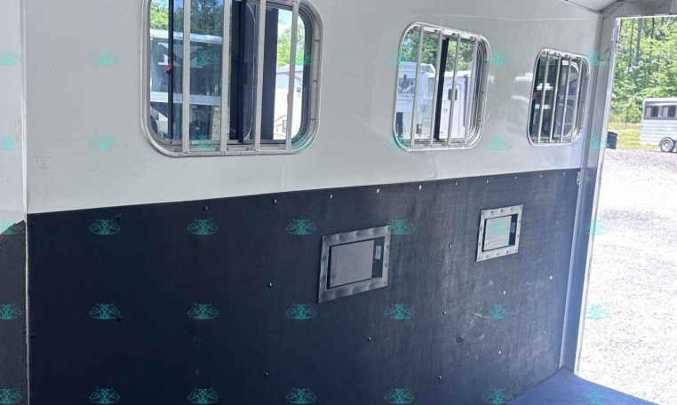 Interior of a horse trailer with white walls, barred windows, and a black lower panel down the side surface.