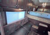 Interior view of a dark wood RV living area with overhead cabinets, a blue upholstered bed with star-patterned pillows, and a brown leather sofa along the wall
