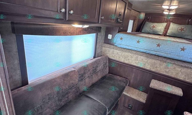 Interior view of a dark wood RV living area with overhead cabinets, a blue upholstered bed with star-patterned pillows, and a brown leather sofa along the wall