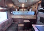 Interior of a trailer showing a raised bed at the back, blue star-pattern bedding, and dark wood cabinets on the sides.