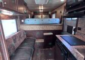 Interior of a dark-wood RV trailer with a sofa on the left, overhead cabinets, and a raised bed toward the back area.