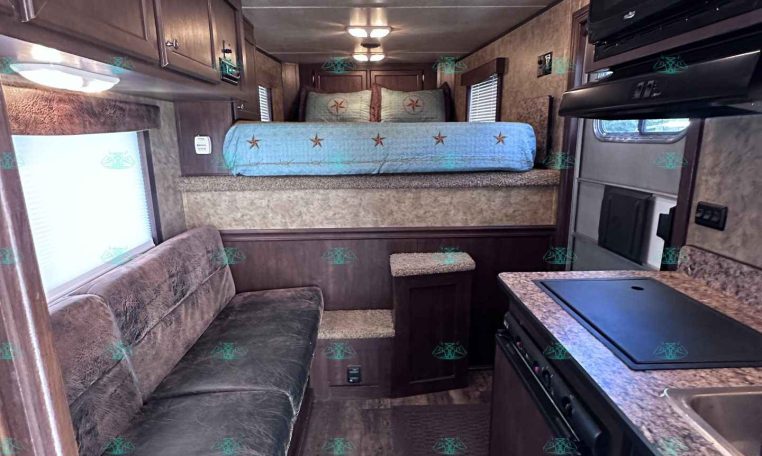 Interior of a dark-wood RV trailer with a sofa on the left, overhead cabinets, and a raised bed toward the back area.