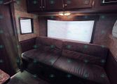RV living area with dark wood cabinets above a burgundy sofa and a window with a shade nearby.