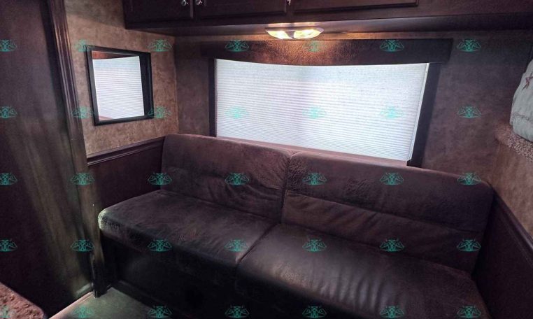 RV living area with dark wood cabinets above a burgundy sofa and a window with a shade nearby.