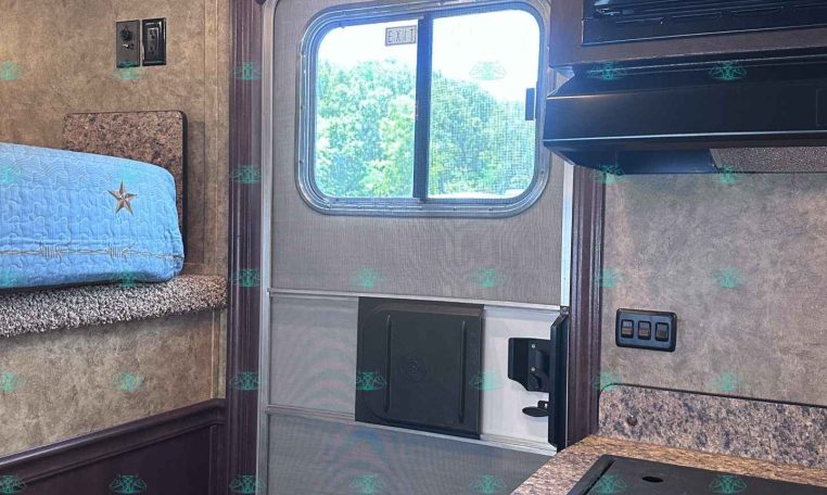 Interior of a small RV/kitchen area with a bunk bed on the left, blue quilt, window in the center, and a microwave above to the right.