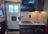 Compact RV kitchen with microwave above the stove, sink, and dark wood cabinets by the entry door