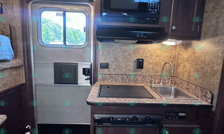 Compact RV kitchen with microwave above the stove, sink, and dark wood cabinets by the entry door