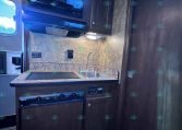 Compact RV kitchen with dark cabinets, granite countertop, microwave, stove, and sink