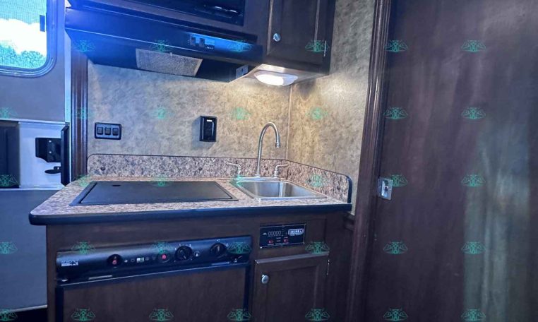 Compact RV kitchen with dark cabinets, granite countertop, microwave, stove, and sink