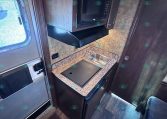 Compact RV kitchen with microwave, stovetop, and sink on a granite counter.