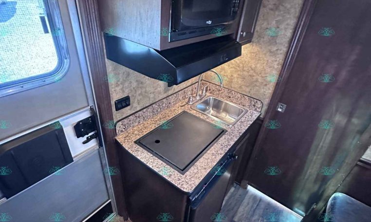 Compact RV kitchen with microwave, stovetop, and sink on a granite counter.