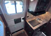 Compact RV kitchen with sink, microwave, and granite countertop beside an exterior exit door windowed by a sliding pane