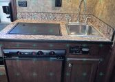 RV kitchen kitchenette with granite countertop, built-in stove, and stainless steel sink.