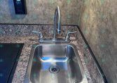 Stainless steel kitchen sink with gooseneck faucet and dual handles set in a granite countertop, showroom backdrop.