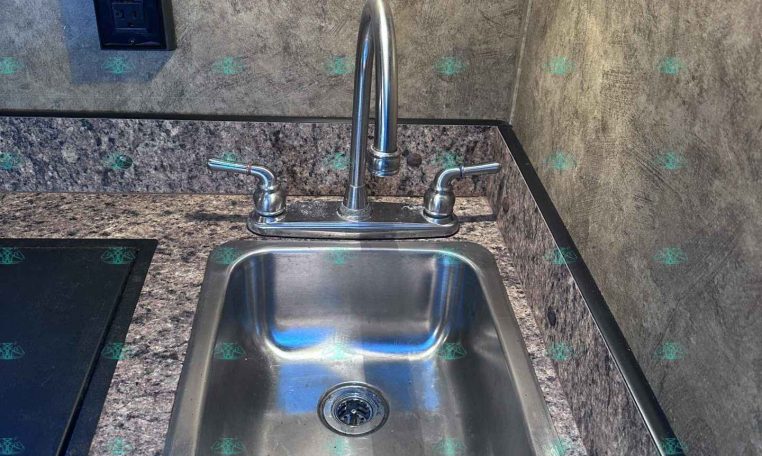 Stainless steel kitchen sink with gooseneck faucet and dual handles set in a granite countertop, showroom backdrop.