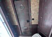 Trailer bathroom with dark wood paneling, beige textured walls, and a frosted door. A circular towel ring hangs on the door above a silver handle.