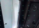 RV bathroom interior featuring a frosted textured glass shower door on the left and a dark wooden door with a towel ring on the right, viewed at a slanted angle.