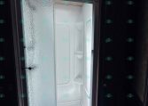 Sliding frosted-glass shower door inside a small bathroom, with a skylight overhead and a white shower enclosure beyond the door