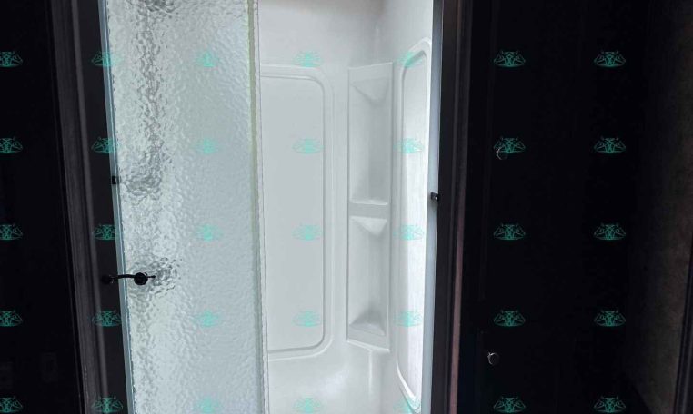 Sliding frosted-glass shower door inside a small bathroom, with a skylight overhead and a white shower enclosure beyond the door