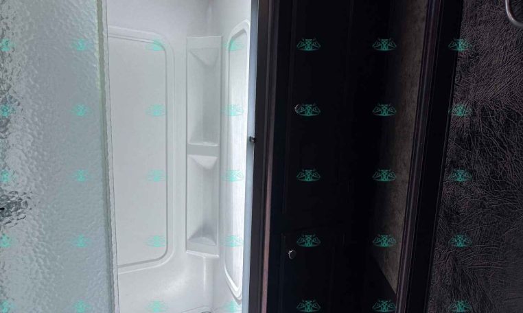 Interior of a trailer bathroom with a white shower stall and frosted glass sliding door, open to a bright outside light from a skylight/roof window.