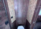 Compact RV bathroom with a tall dark wood cabinet, brown textured walls, and a white toilet.