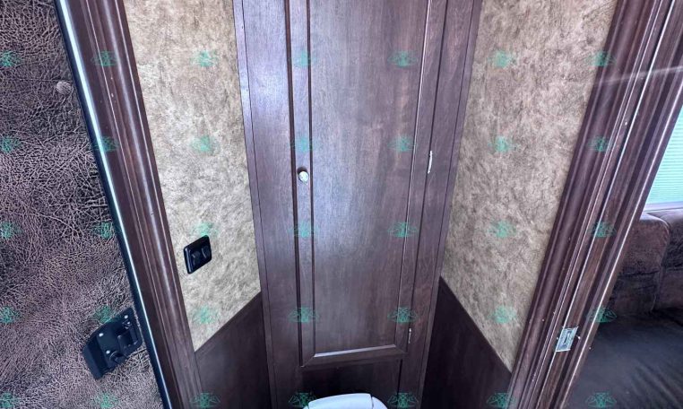 Compact RV bathroom with a tall dark wood cabinet, brown textured walls, and a white toilet.