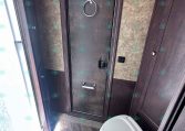 Bathroom inside a trailer: dark wood panel door with a circular towel ring and a white toilet nearby, compact and organized space.
