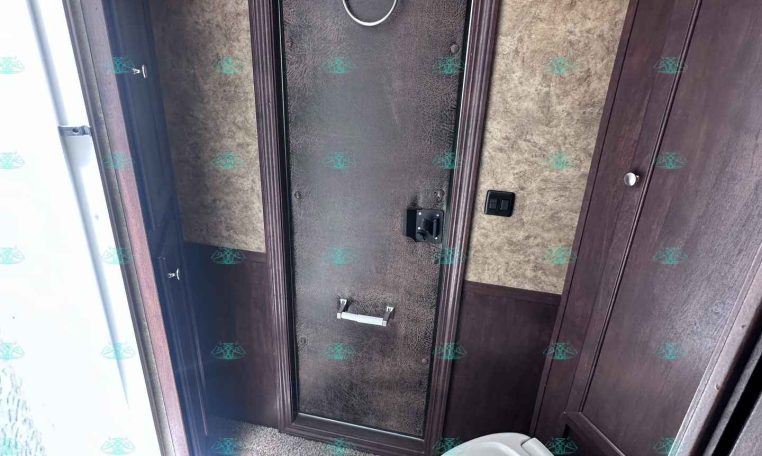 Bathroom inside a trailer: dark wood panel door with a circular towel ring and a white toilet nearby, compact and organized space.