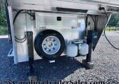 Interior of a camping trailer's undercarriage showing a mounted spare tire, two propane tanks, and electrical components/boxes.