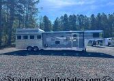 Large gray travel trailer parked on a gravel lot with a forest of tall pines in the background, under a clear blue sky.