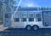 Silver horse trailer with open side windows and ramp down, parked on gravel with trees and blue sky in background; shows 'SMC Trailers' branding and website at bottom.