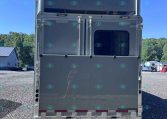 Rear view of a large silver semi-trailer parked on a gravel lot under a clear blue sky.