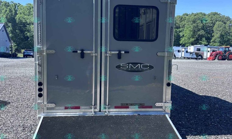 Rear view of a silver trailer with dual rear doors and lowered loading ramp on a gravel lot; 'SMC Trailers' logo visible on doors.