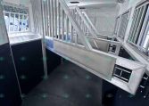 Interior of aluminum horse trailer showing ramp-style stairs, dividers, and ventilation windows for horses alternating with dark stall walls on the sides.