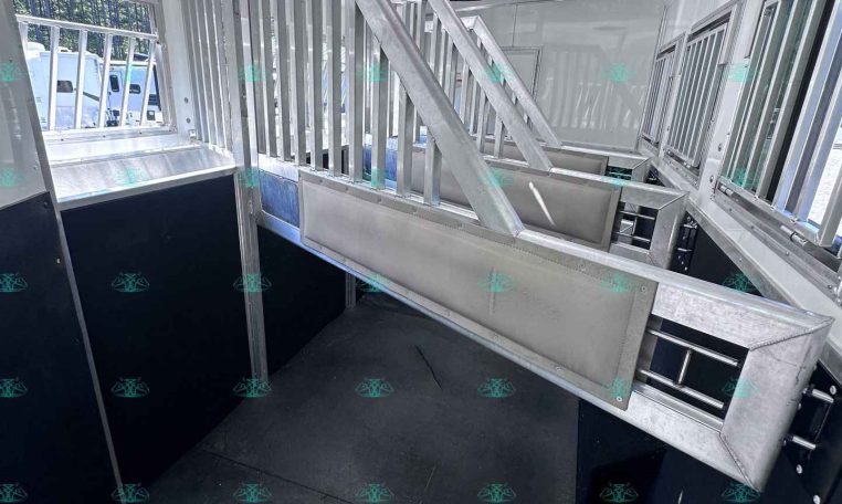 Interior of aluminum horse trailer showing ramp-style stairs, dividers, and ventilation windows for horses alternating with dark stall walls on the sides.