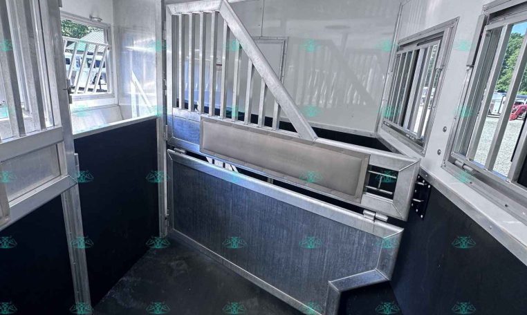 Interior of a stainless horse trailer with metal dividing partitions and a slanted floor ramp for loading horses or livestock.