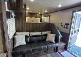 Interior of a wood-paneled RV living area with a black leather sofa and patterned cushions beneath built-in cabinets in warm lighting.