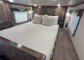 A cozy RV bedroom with a large white bed, decorative pillows, and dark wood cabinets along the walls.