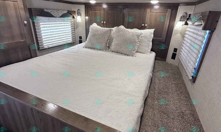 A cozy RV bedroom with a large white bed, decorative pillows, and dark wood cabinets along the walls.