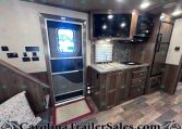 Interior view of a modern RV kitchen with wood cabinetry, stainless steel appliances, and a tiled backsplash.