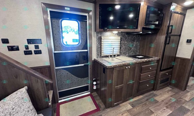 Interior view of a modern RV kitchen with wood cabinetry, stainless steel appliances, and a tiled backsplash.