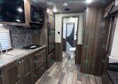 Interior of a modern RV kitchen with dark wood cabinets, marble-style backsplash, microwave, stove, and fridge.